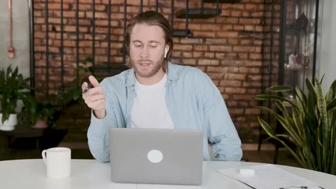 Young handsome blond man sitting at his desk with a laptop communicates by video Stock Footage 239652443