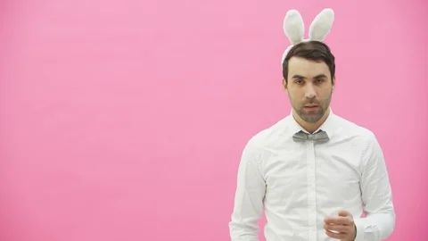 Young handsome boy standing on a pink background. A man with rabble ears on his Stock Footage 104688533