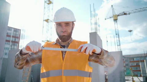 Young handsome builder in a hardhat holds a tape measure ruler in his hands Stock Footage 241172641