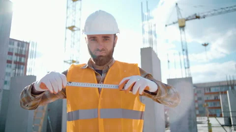 Young handsome builder in a hardhat holds a tape measure ruler in his hands Stock Footage 247771144