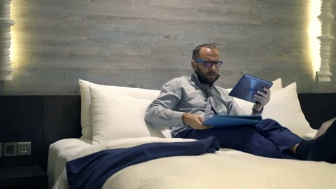 Young, handsome businessman with documents and tablet computer lying on bed, 4K Stock Footage 71280073