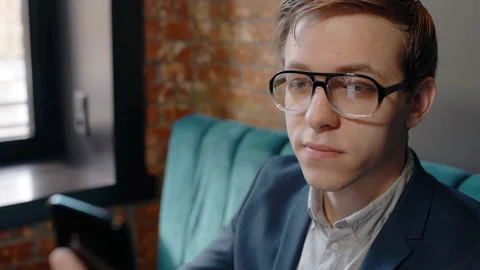Young handsome businessman is using smartphone, sitting at table in cafe, guy in Stock Footage 88570587