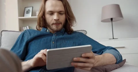 Young handsome caucasian guy with long hair in denim shirt plays video game Stock Footage 147050597