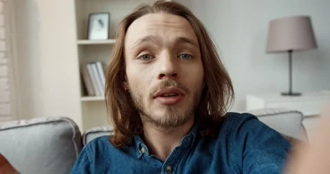 Young handsome caucasian guy with long hair in denim shirt is talking on video Stock Footage 147050599