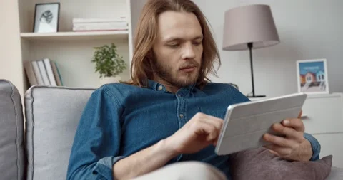 Young handsome caucasian guy with long hair in denim shirt browses news on Stock Footage 147050607