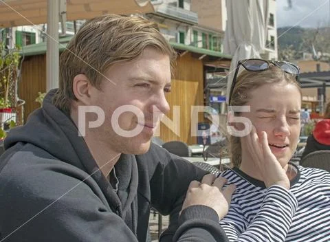 Young handsome couple sit in cafe and squint in stark sunshine Stock Photos