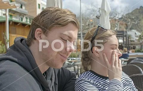 Young handsome couple sit in cafe and squint in stark sunshine Stock Photos