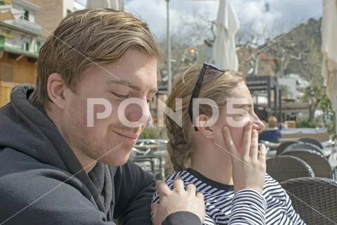 Young handsome couple sit in cafe and squint in stark sunshine Stock Photos