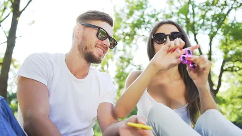 Young handsome couple sitting on the grass in the park and using hand spinners Stock Footage 87911224