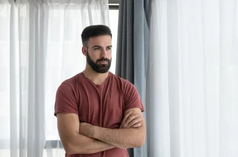 Young handsome depressed man standing alone and looking through the window Stock Photos