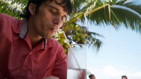 Young handsome enjoying man drinking water in beach cafe sitting by sea on palm Stock Footage 85094109