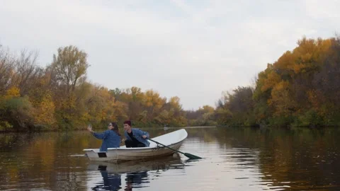 Young handsome guy and a beautiful girl takes a photo in a boat on a lake in a Stock Footage 143644859