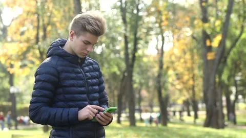 Young handsome guy in a blue jacket uses a mobile phone. Stock Footage 142137952