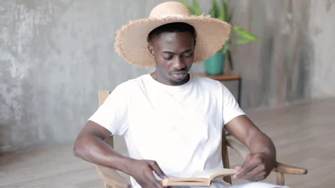 A young handsome guy in a hat of African American appearance is reading a book.  Stock Footage 203971423