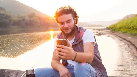Young handsome guy makes selfie, talks on Skype, smiles, sitting in a wooden 스톡 동영상 81759693
