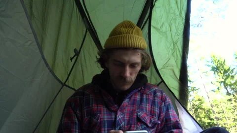 Young handsome guy with a mustache and a beard prepares a tent and a sleeping Stock Footage 130196554