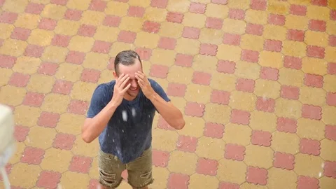 A young handsome guy rejoices in the rain by lifting his hands up and washing Видео 80331497