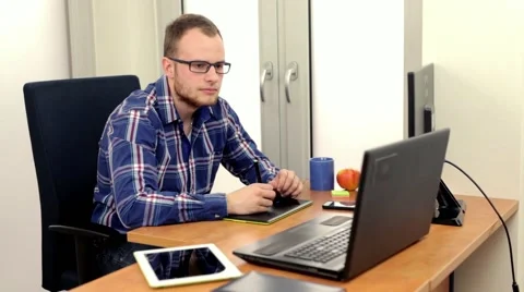 Young handsome guy sitting behind the desk and using his two computers Stock Footage 49058091