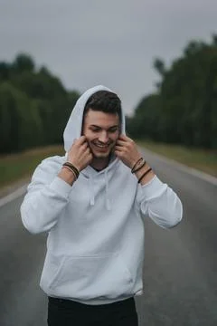 A young handsome guy with a small beard in a white jacket walks along the road Stock Photos