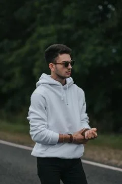 A young handsome guy with a small beard in a white jacket and dark glasses is Stock Photos