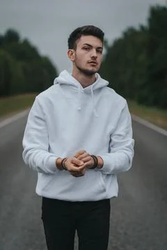 A young handsome guy with a small beard in a white jacket is walking along the Stock Photos
