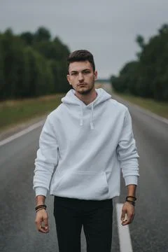 A young handsome guy with a small beard in a white jacket walks along the road Stock Photos