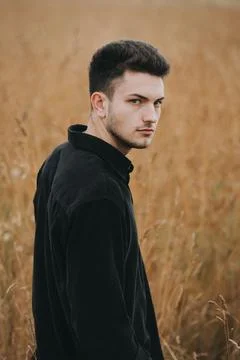 A young handsome guy with a small beard in a black shirt looks at the camera Stock Photos