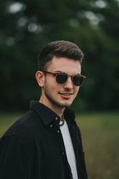 A young handsome guy with a small beard in a black shirt and dark glasses looks Stock Photos