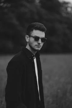 A young handsome guy with a small beard in a black shirt and dark glasses looks Stock Photos