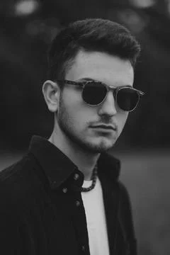 A young handsome guy with a small beard in a black shirt and dark glasses looks Stock Photos