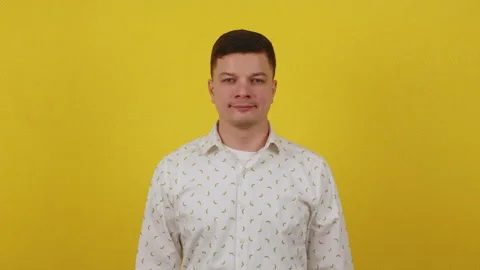 A young handsome guy stands on a yellow background in a shirt and smiles Stock Footage 172044396