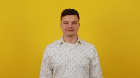 A young handsome guy stands on a yellow background in a shirt and smiles Stock Photos