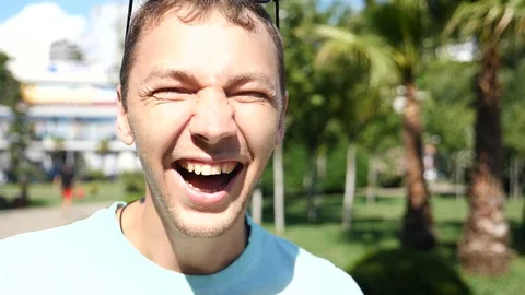 Young handsome guy in summer park laughs looking at camera. Slow motion Stock Footage 77444019