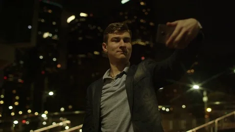 Young handsome guy is taking a few selfies on a midnight street Stock Footage 77578262