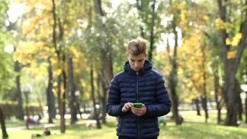 Young handsome guy walk and uses a mobile phone while in the autumn public park. Video stock 142136195