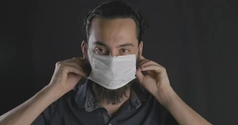 Young handsome guy is wearing face mask in studio shot, black background. Pro Stock Footage 139825399