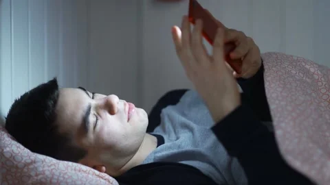 Young Handsome Hipster Man using a Smartphone Lying on Bed at Home Late at Night Video stock 130930342