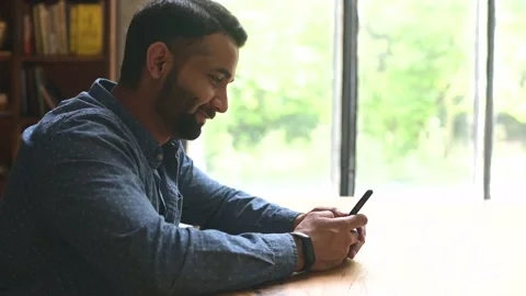Young handsome Indian freelancer man using smartphone for online chatting Video stock 158799103