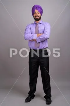 Young handsome Indian Sikh businessman wearing turban against gr Stock Photos