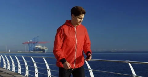 Young handsome jogging on the sea dock and taping on his phone in the nice blue Stock Footage 82286249