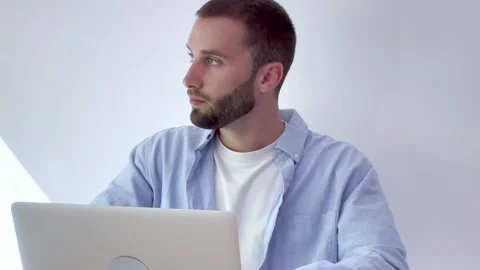 Young handsome man with a beard looking thoughtful while working on his laptop Video stock 346822757