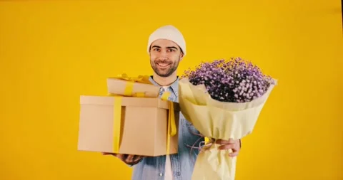 Young handsome man with big present box and bunch of flowers on yellow backgr Stock Footage 170654683