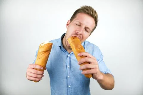 Young handsome man biting half of french baguette looking hungry on isolated Foto stock
