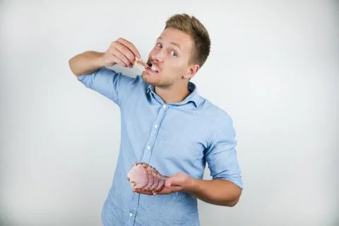 Young handsome man biting slice of bacon on isolated white background Foto stock