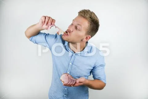 Young handsome man biting slice of bacon with hunger on isolated white Stock Photos
