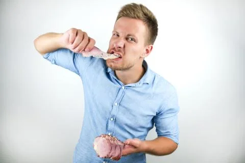 Young handsome man biting slice of bacon with hunger looking wild on isolated Stock Photos