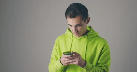 Young handsome man in a bright sweater using smartphone on grey studio Video stock 147562059