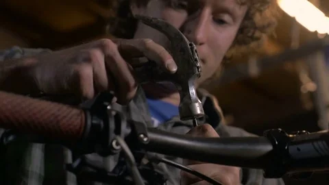 A young handsome man carefully uses a hammer to repair mountain bike Stock Footage 69907690