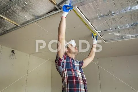 Young handsome man in casual clothing takes measurement of drywall suspended Stock Photos