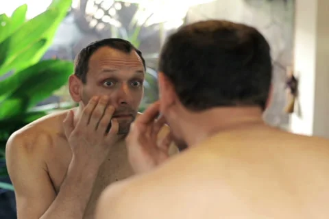 Young, handsome man checking his wrinkles in the bathroom NTSC Stock Footage 39619205
